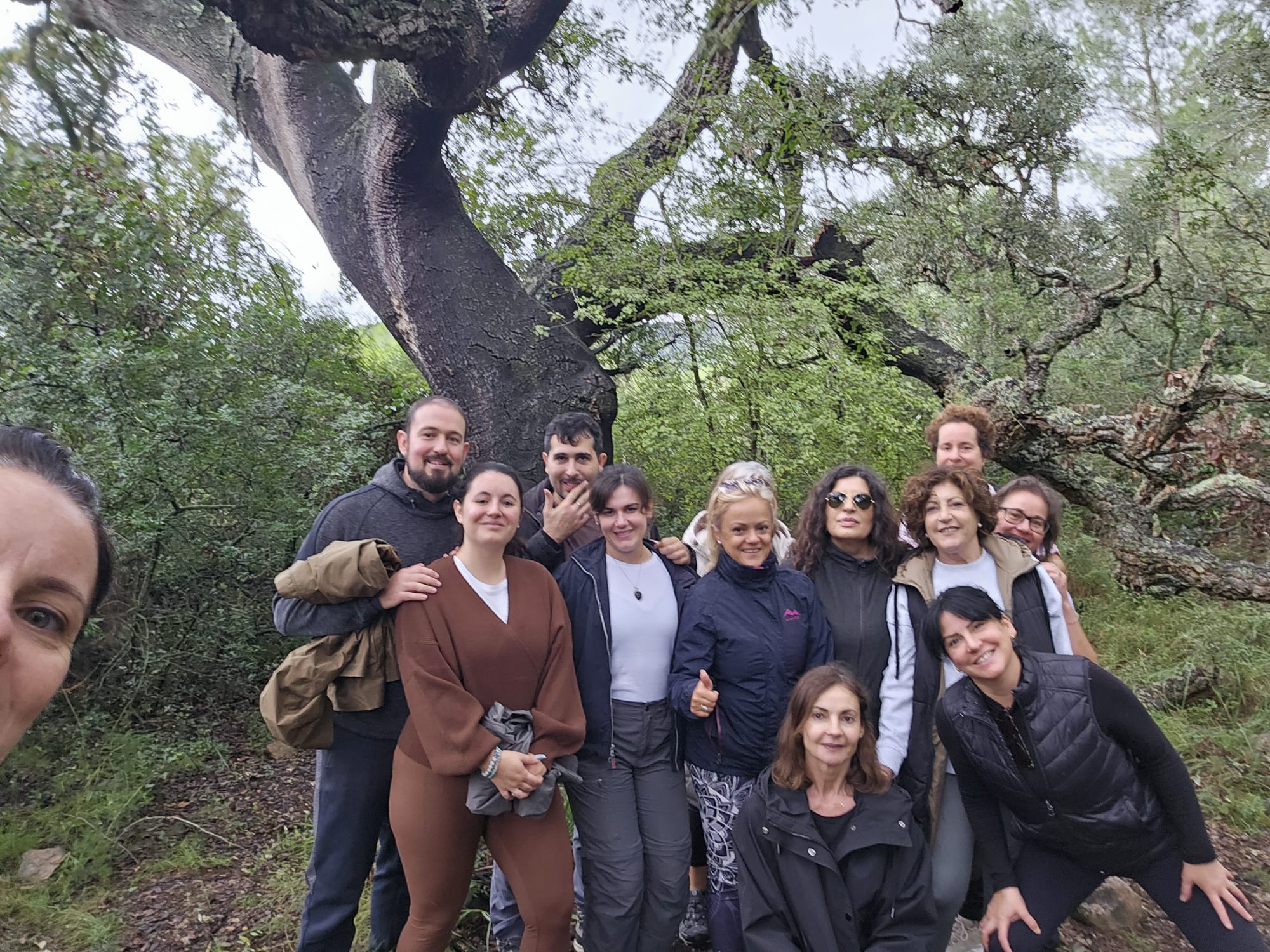 El grupo del retiro posando bajo un alcornoque enorme en la Sierra de Espadán, con el bosque mojado detrás