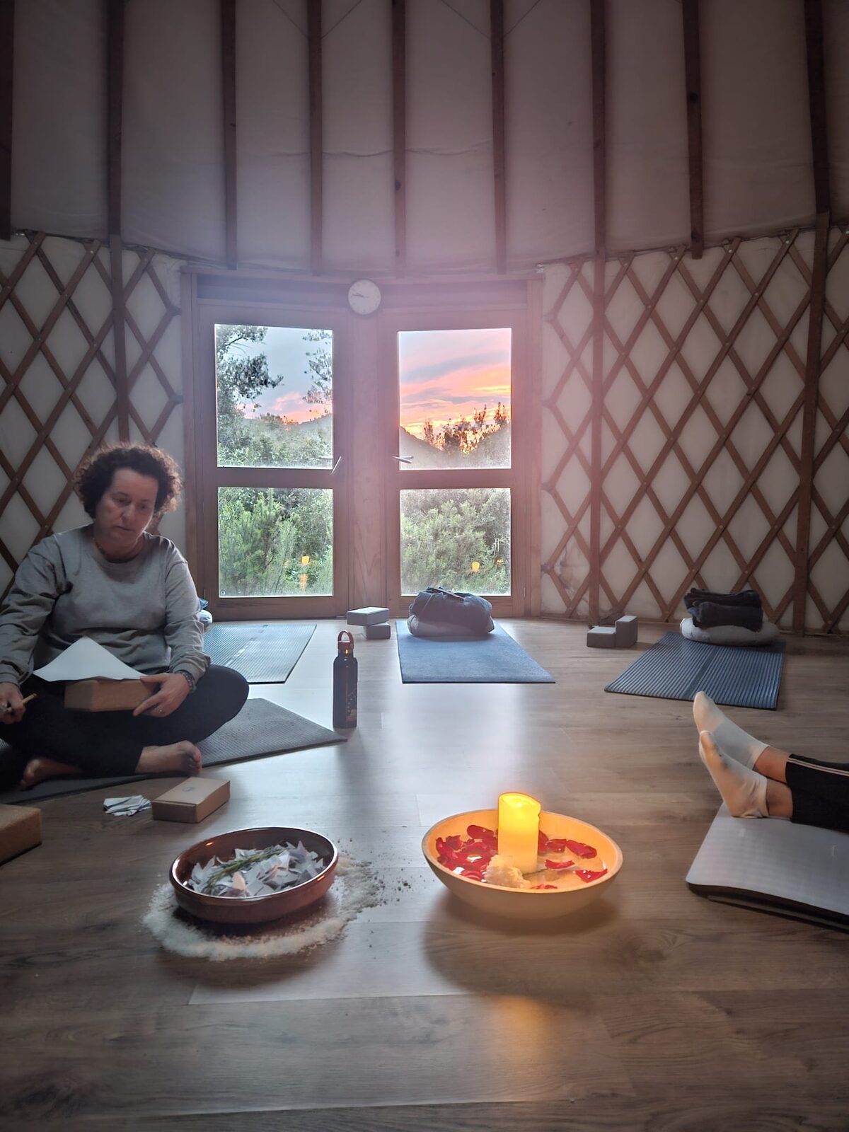 Una participante del retiro escribiendo su contrato sentada en el suelo de la yurta, junto al cuenco con la vela, con el atardecer en la ventana