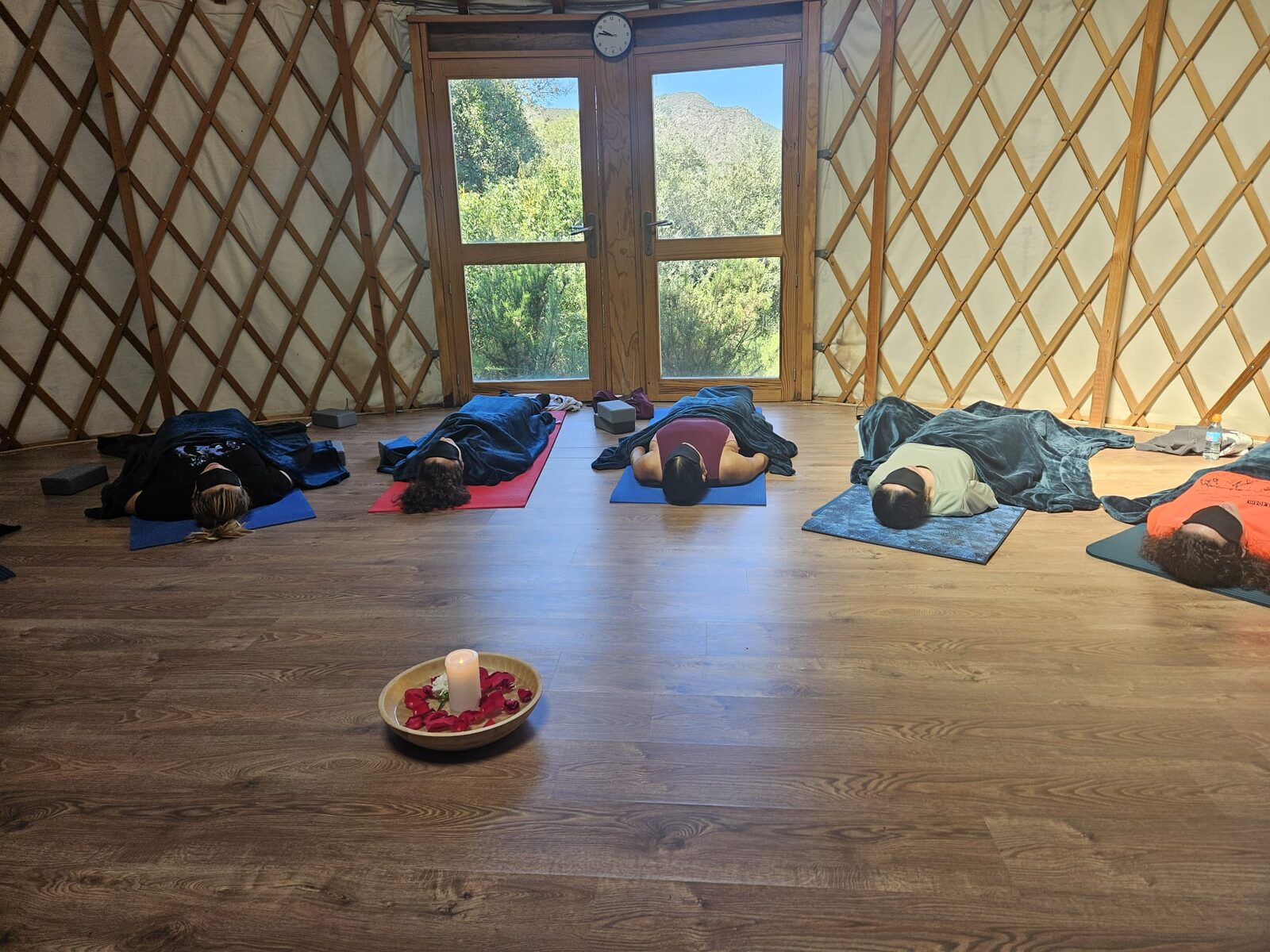 El grupo en savasana, tumbado sobre las esterillas de la yurta con la vela y los pétalos en el centro del círculo