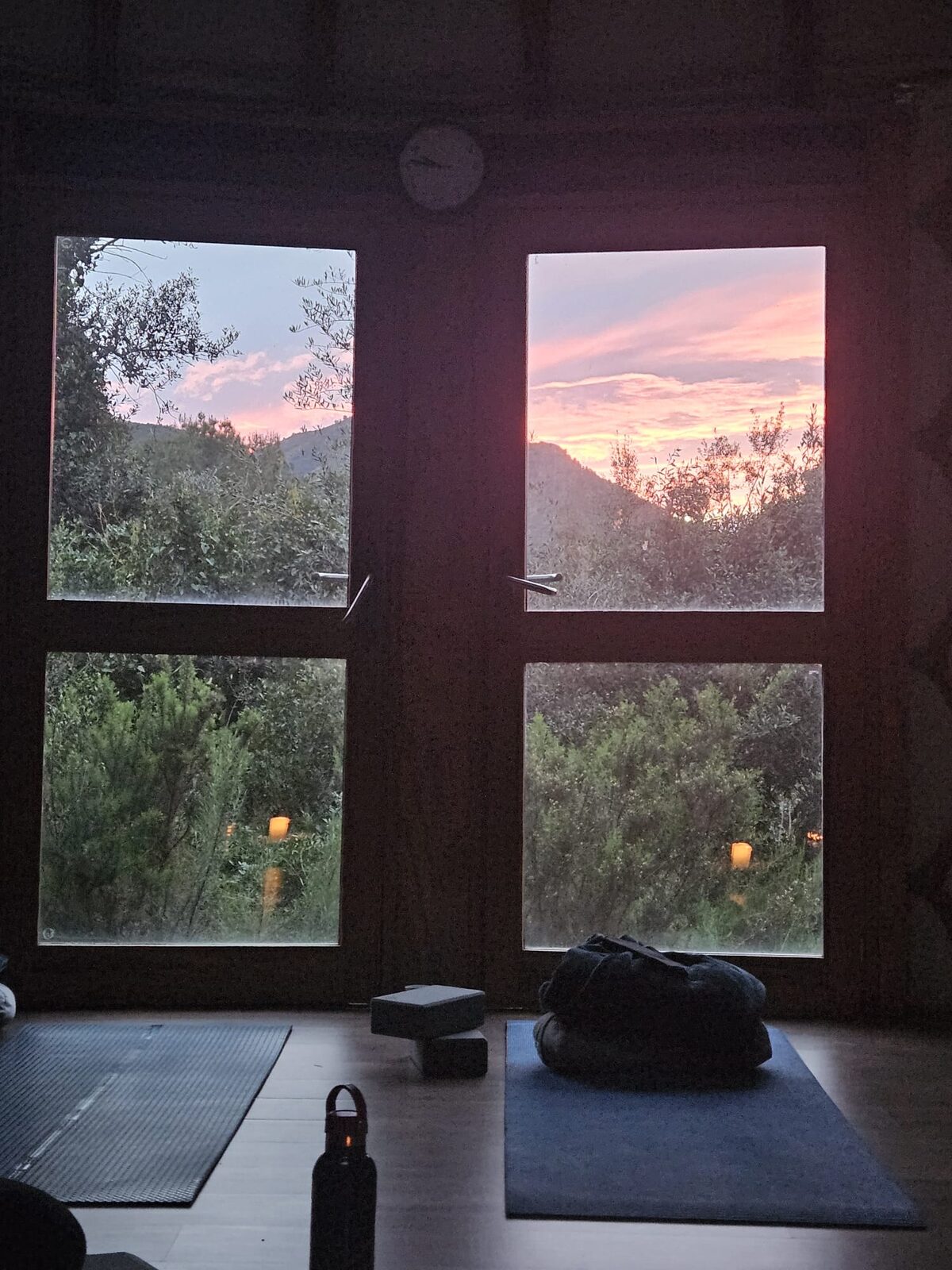 El ventanal de la yurta de Mar de Fulles al atardecer, con el cielo rosa sobre el bosque y las esterillas preparadas en el suelo
