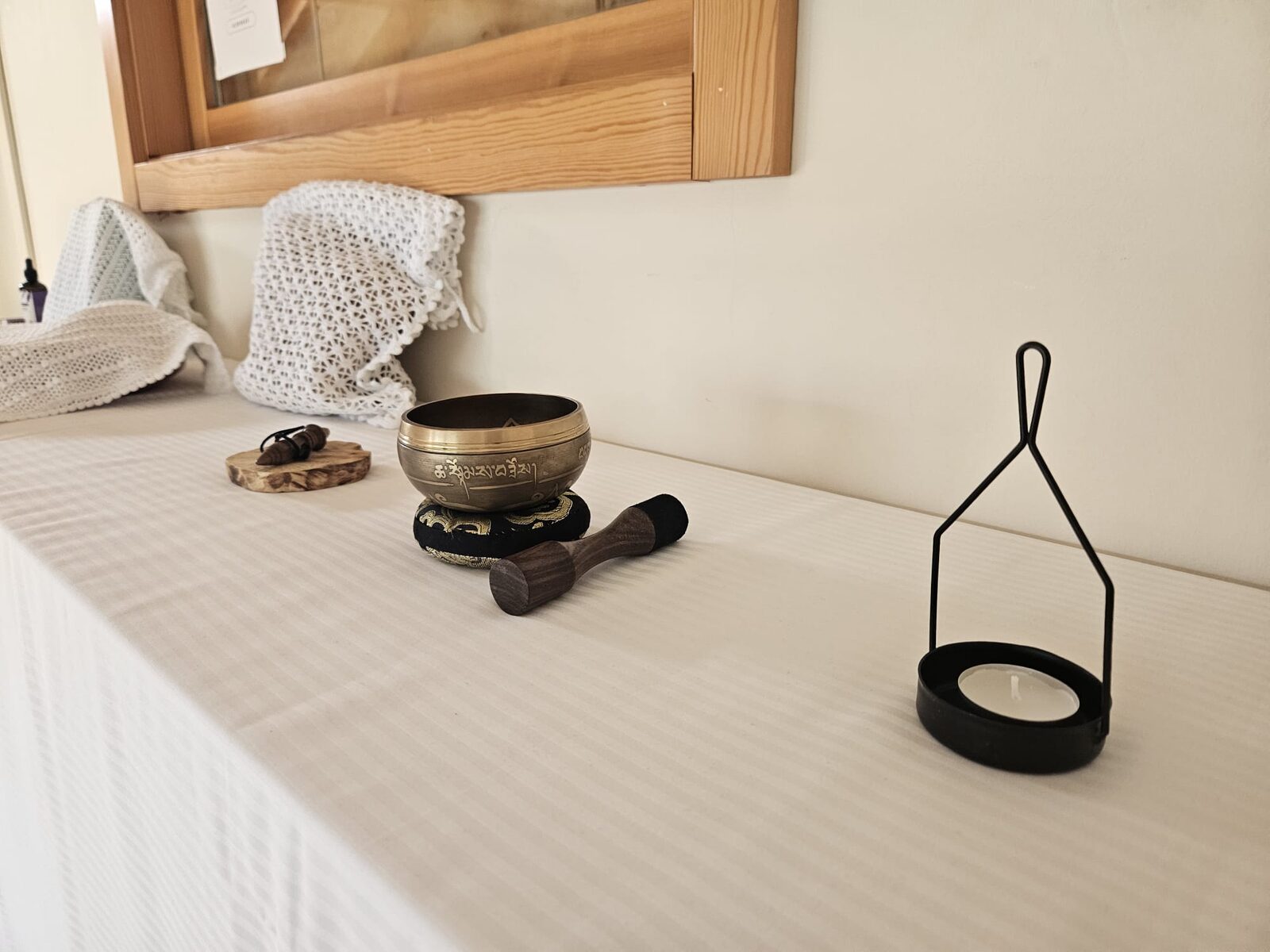 Un cuenco tibetano con su maza sobre la mesa del taller, junto a un portavelas negro