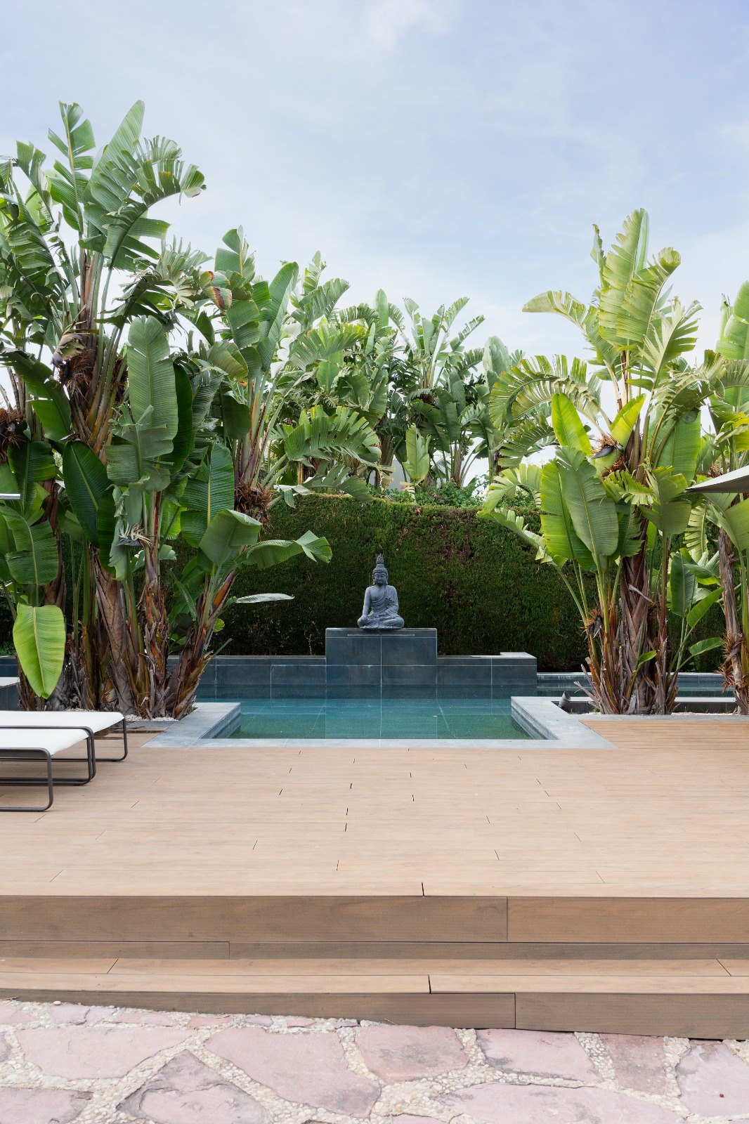 La piscina del jardín con una figura de Buda al fondo, rodeada de plataneras